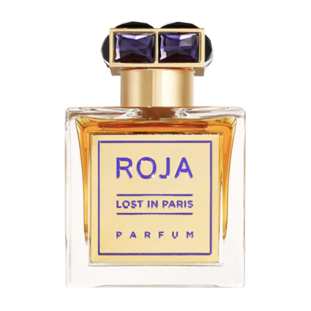 A square-shaped perfume bottle with a clear glass body and a gold-colored cap with purple accents. The label reads 'ROJA LOST IN PARIS PARFUM'.